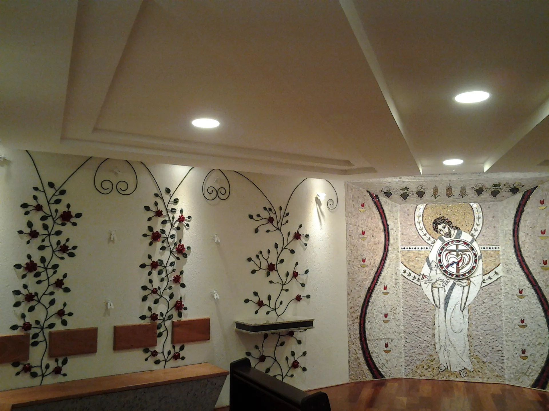 Parede lateral da Capela do Santíssimo com roseiras e abelhas brancas em metal, ao lado do mosaico