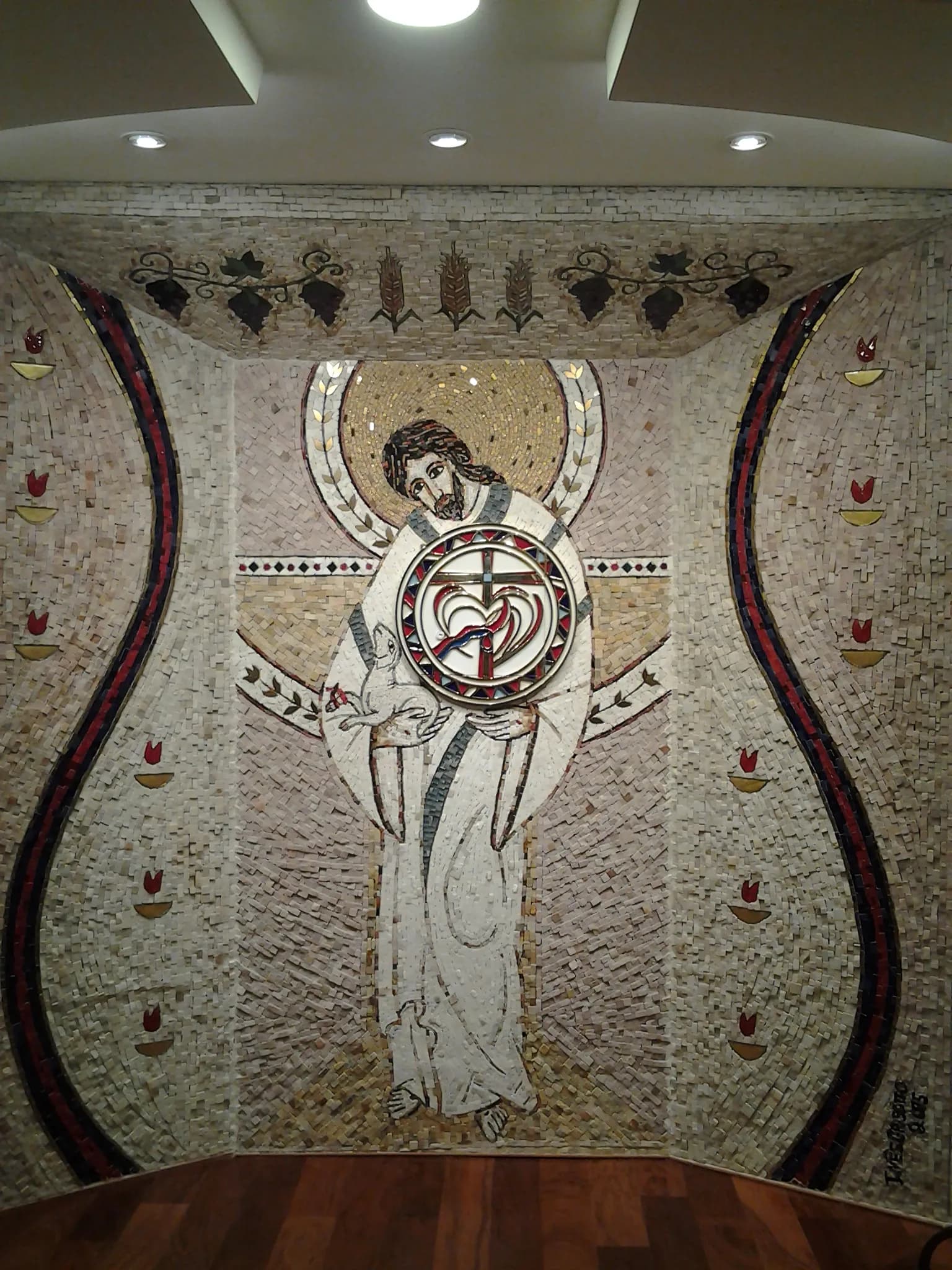 Mosaico da Capela do Santíssimo visto de frente, com uvas e espigas em metal no topo e chamas nas laterais